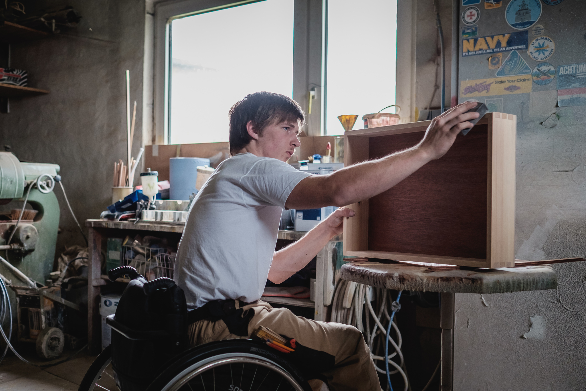 Ein junger Mann im Rollstuhl arbeitet in einer Tischlerwerkstatt an einer Schublade