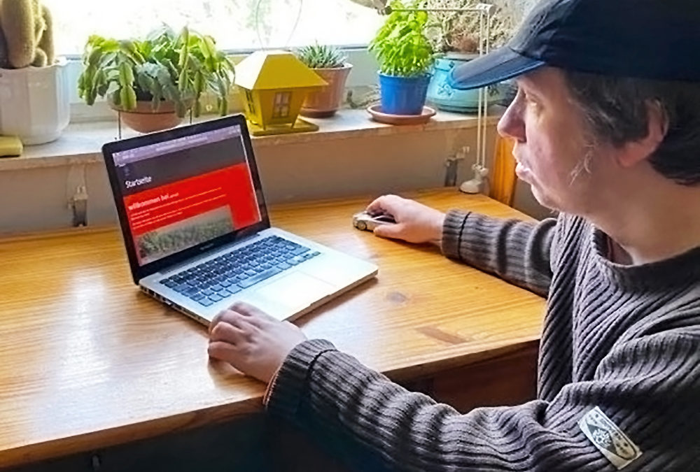 Dirk Hähnel sitzt am Tisch Laptop. Auf dem Monitor ist die Website von uLPeDi zu sehen