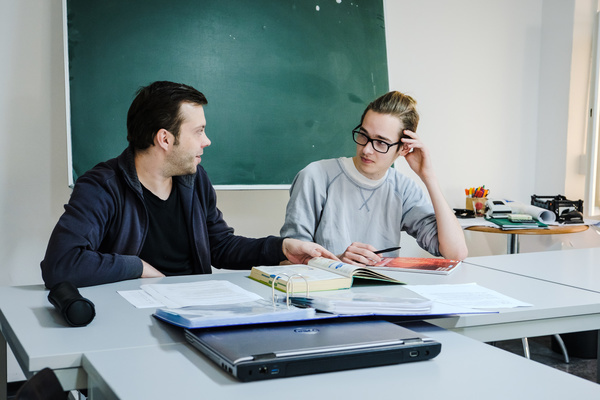 Eine Lehrperson und ein Azubi sitzen vor einer Tafel und üben gemeinsam.