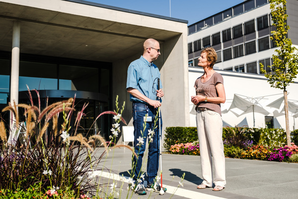 Zwei Menschen stehen vor einem Bürogebäude und unterhalten sich.