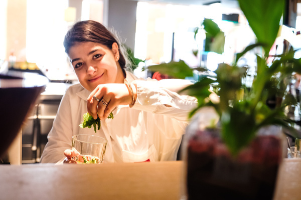 Eine junge Frau mit Lernschwierigkeiten arbeitet in einer Bar. Sie streut Minze in ein Glas und schaut in die Kamera